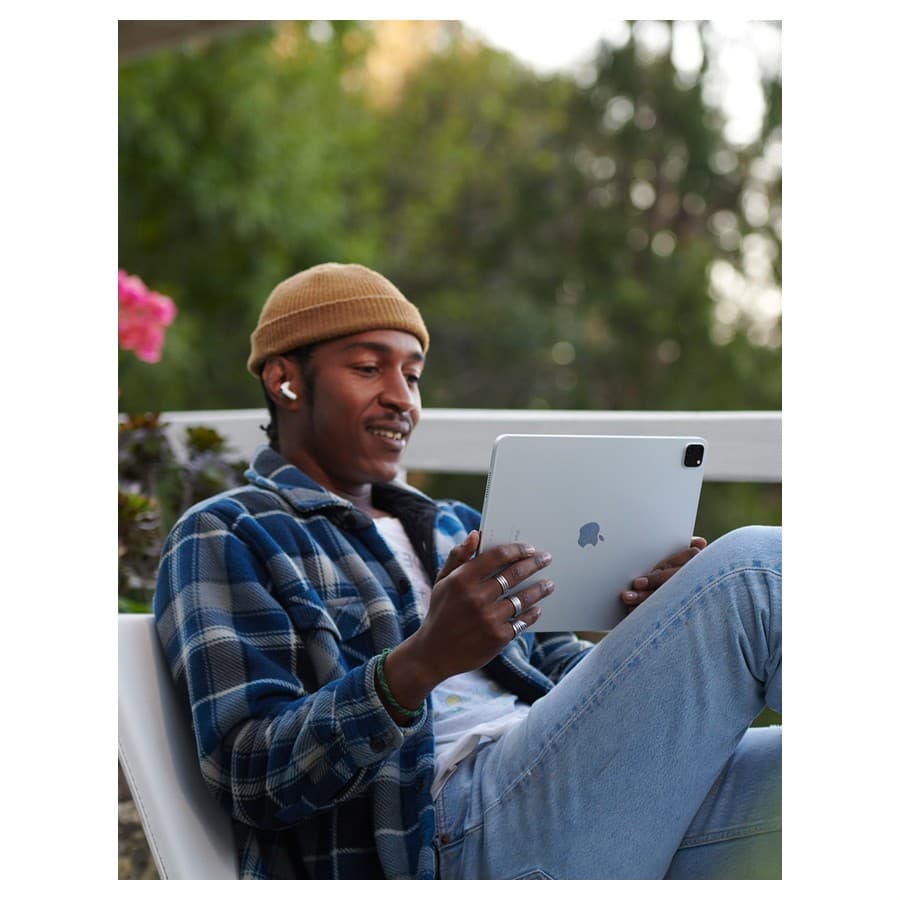 Person sitting outdoors, looking at an iPad, listening to AirPods Apple sale