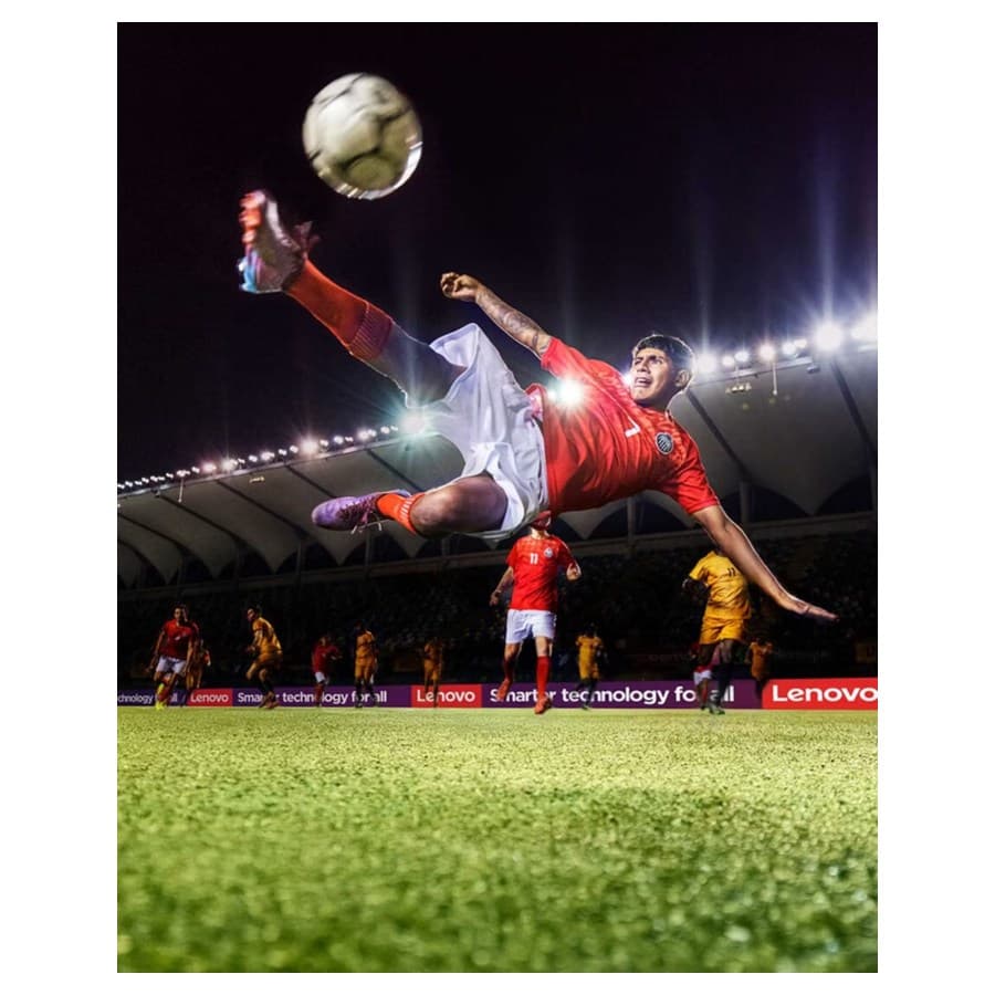 Young man at FIFA performing the bicycle kick soccer move with players in the background. Lenovo sale